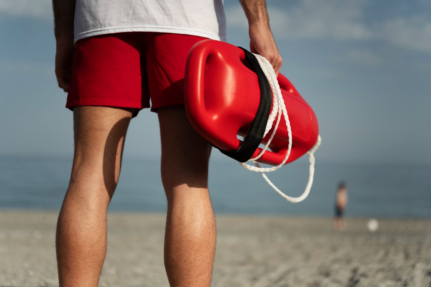 Lifeguard in red shorts carrying a rescue can along the beach