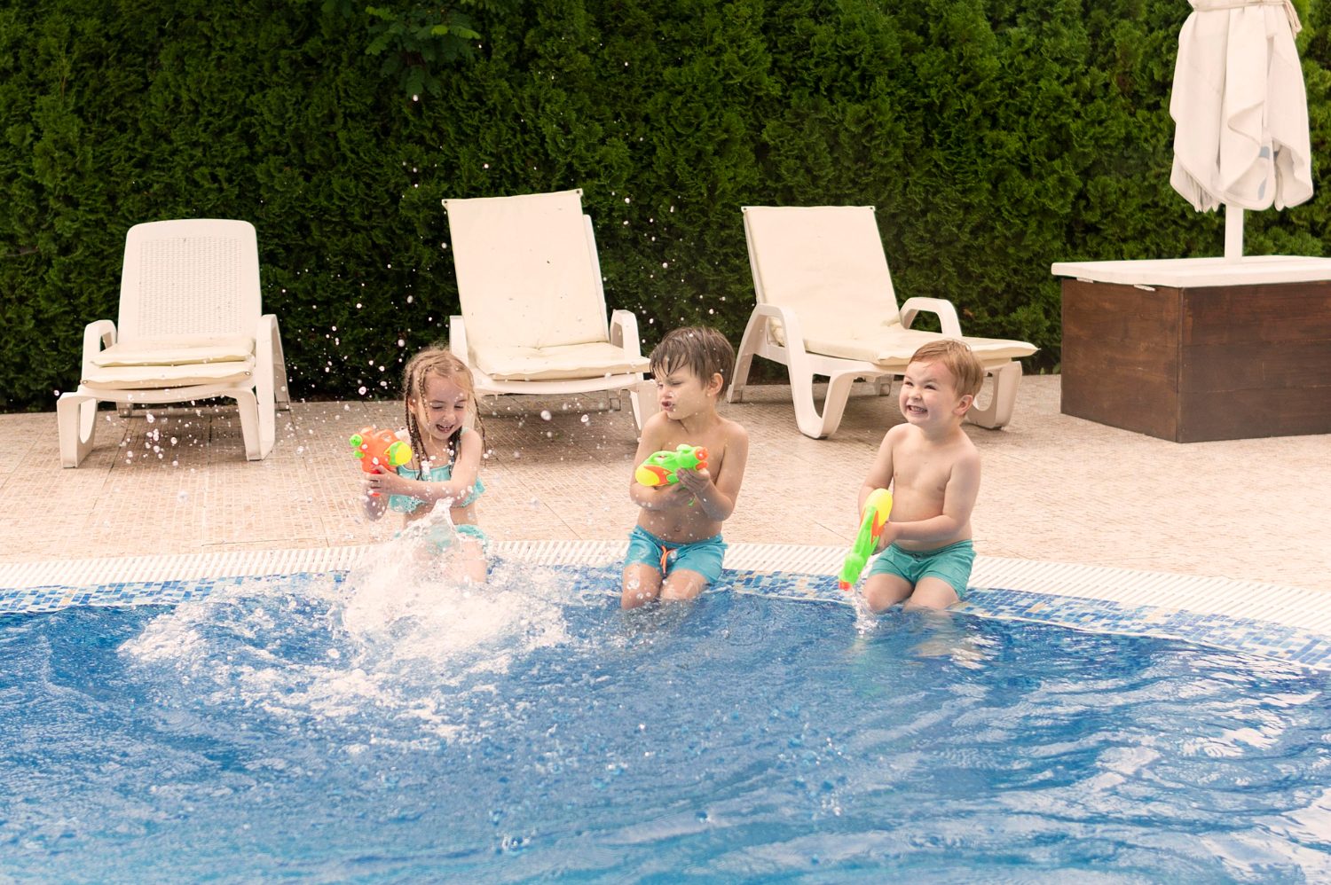 Children relaxing on inflatable rings at a backyard pool party while a lifeguard watches