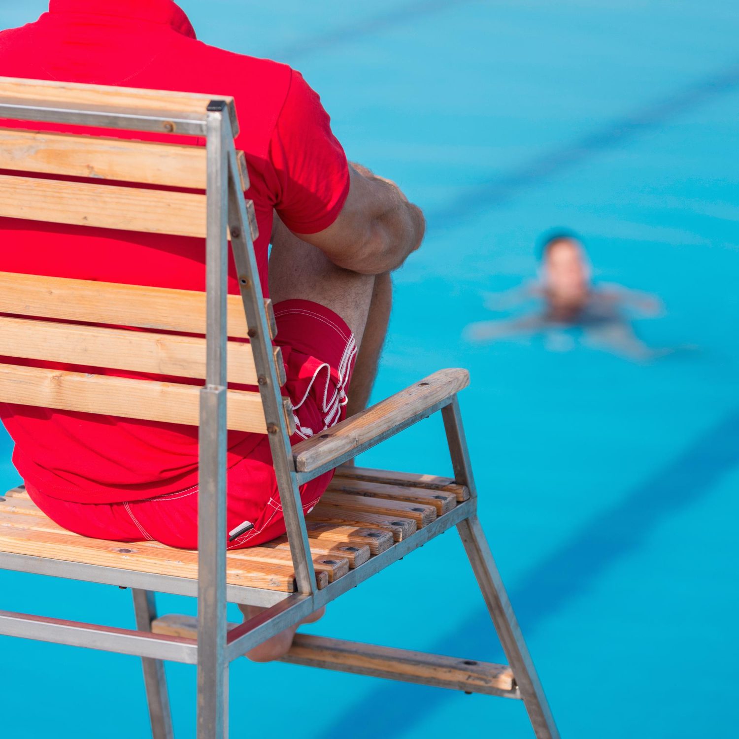 Two lifeguards on duty beside a pool full of swimmers