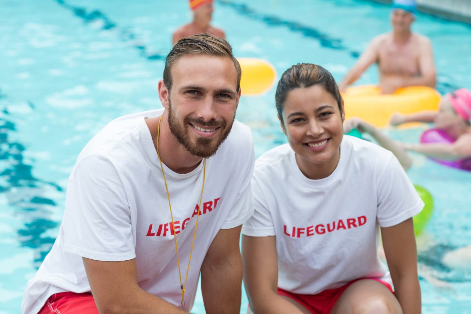 Two uniformed lifeguards standing together beside a swimming pool