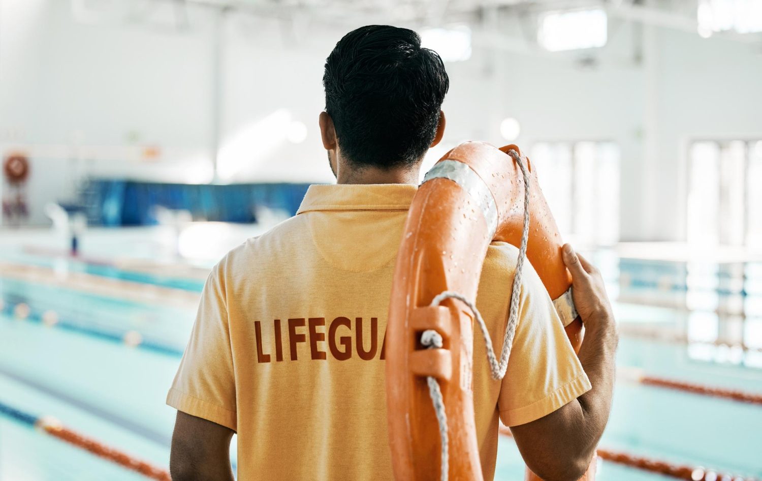 Lifeguard with a rescue tube watching swimmers in an indoor lap pool