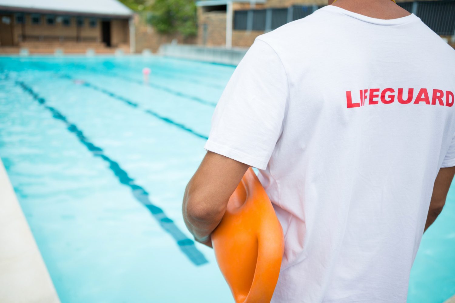 Lifeguard carrying a rescue buoy at an outdoor pool